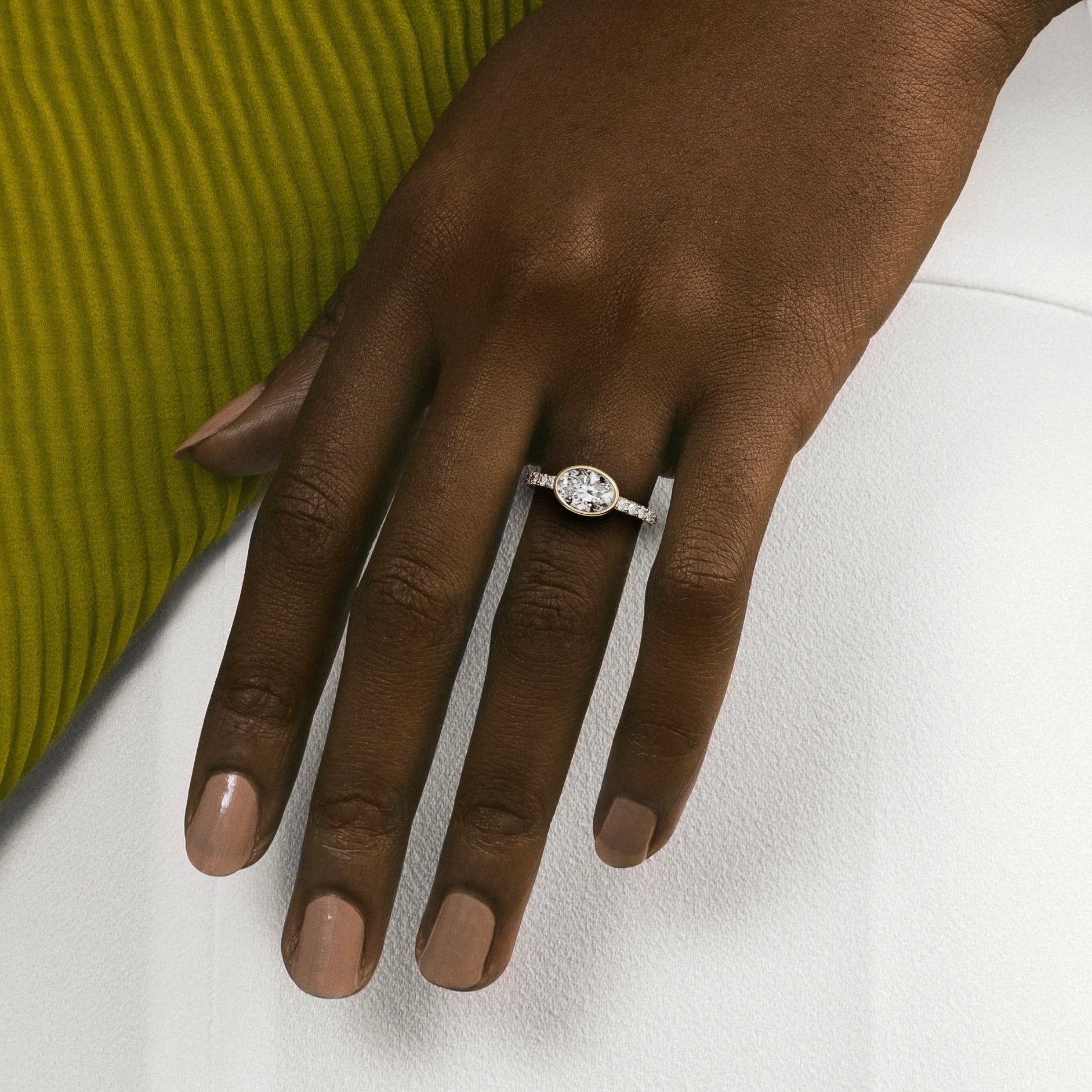 Close view of east-west oval diamond bezel engagement ring with pavé diamond band