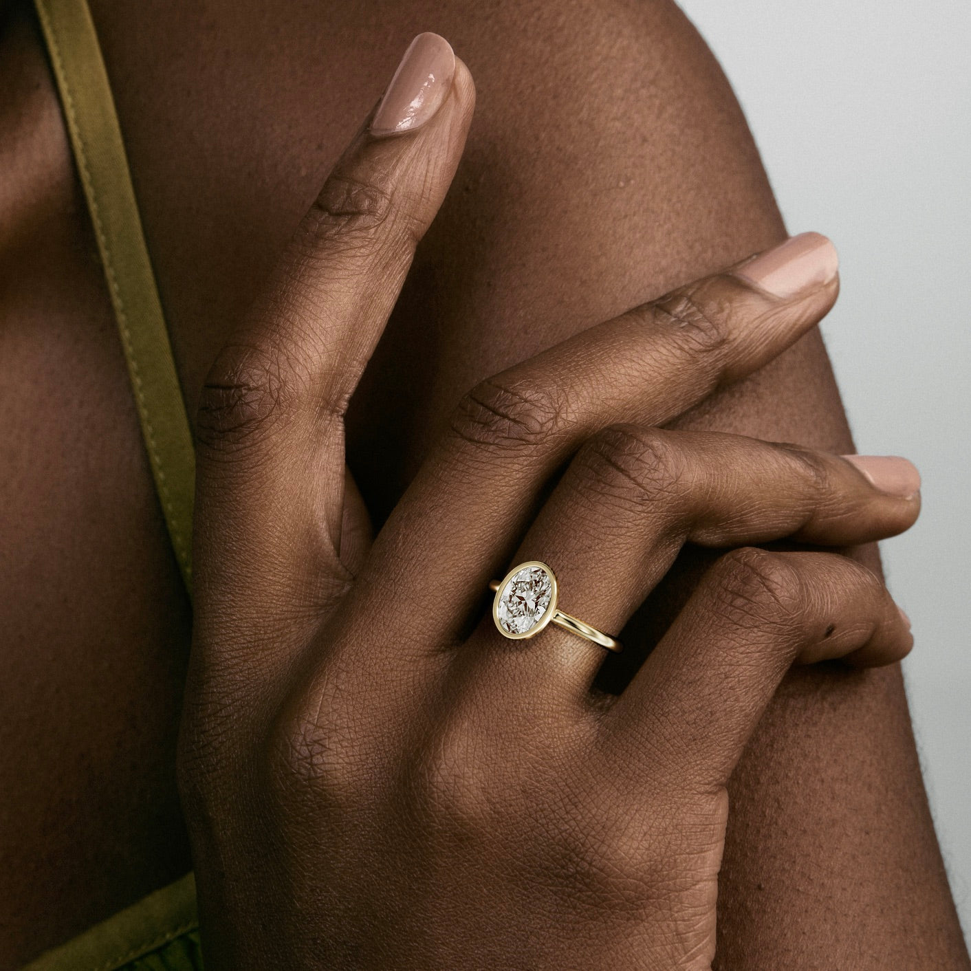 close view of 1.50 ct oval diamond bezel engagement ring on thin domed band worn on hand