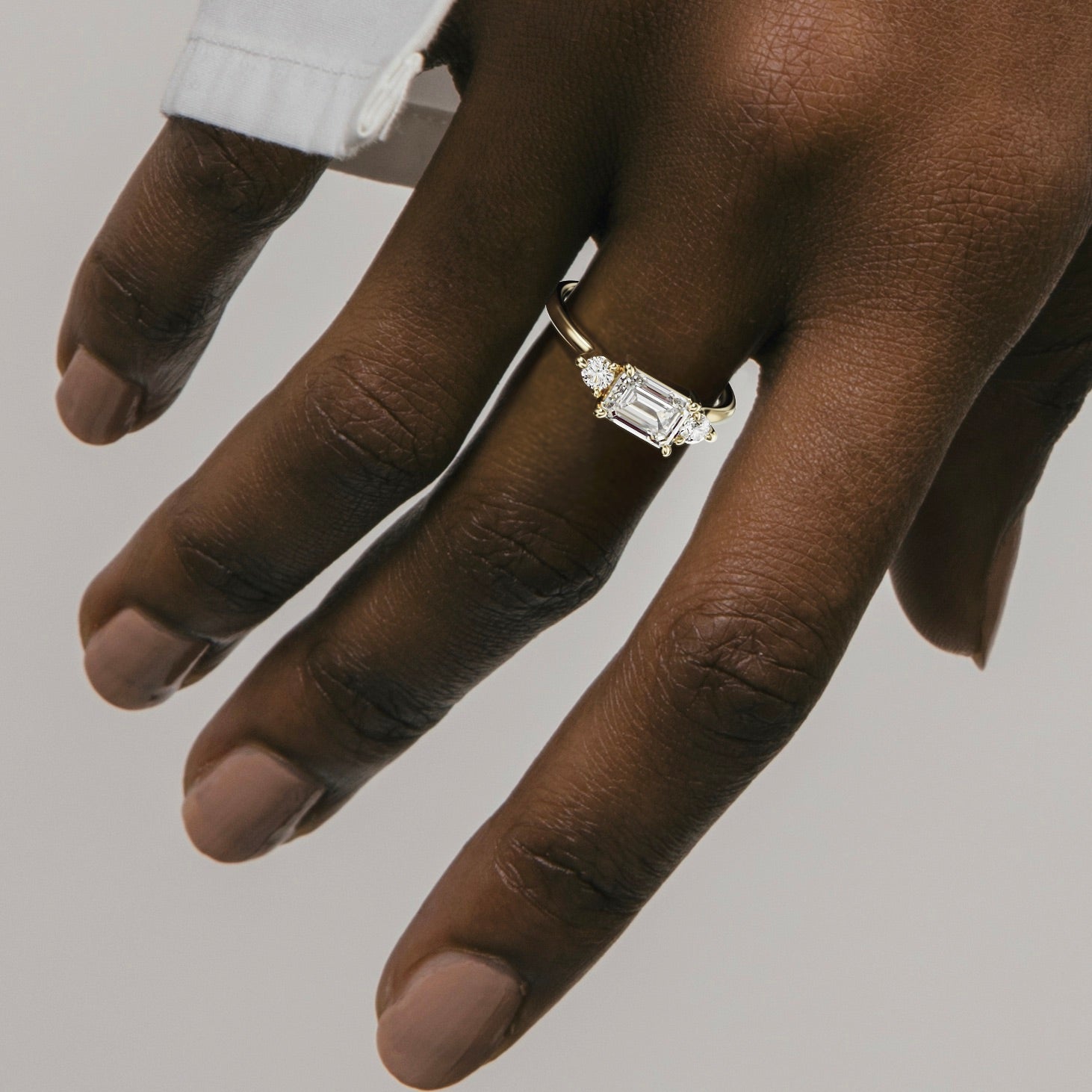 Kala 1.50 carat east west emerald diamond three stone ring close hand detail