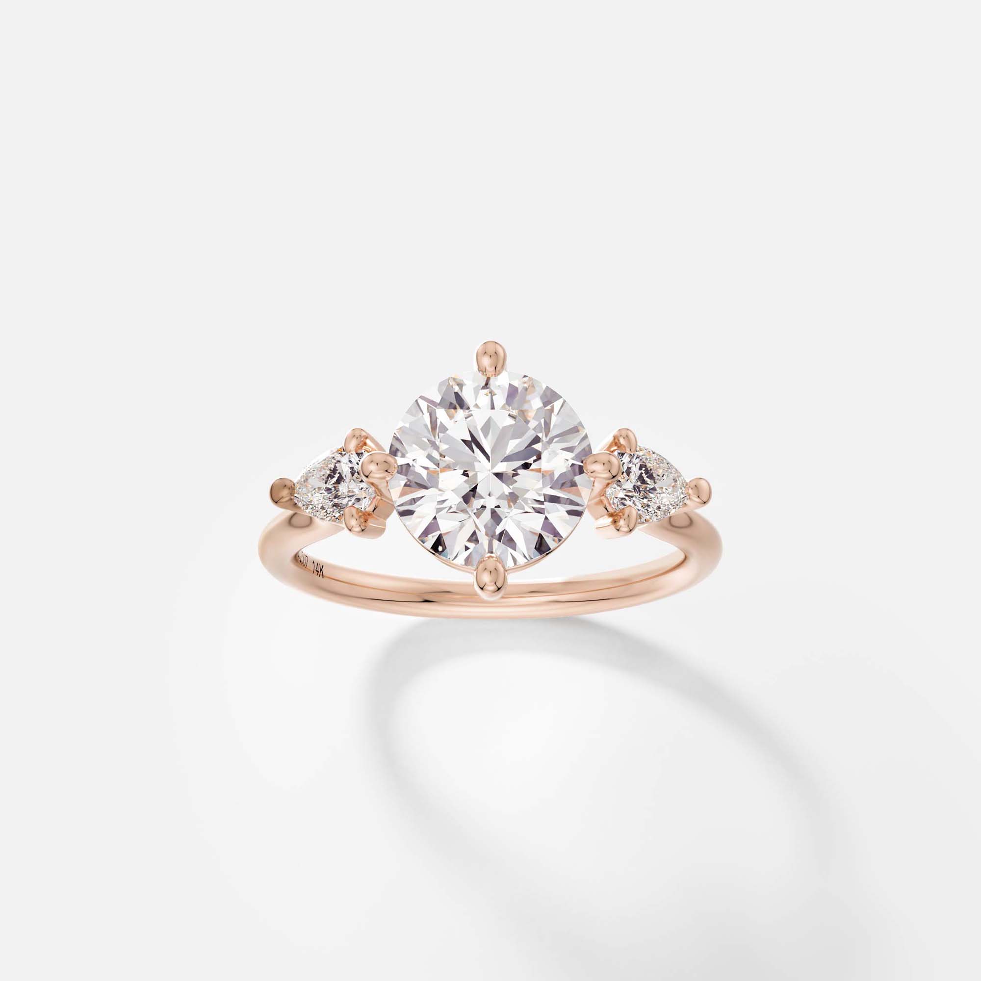 14k rose gold three stone engagement ring with 2 carat round diamond and pear side stones on delicate round profile band