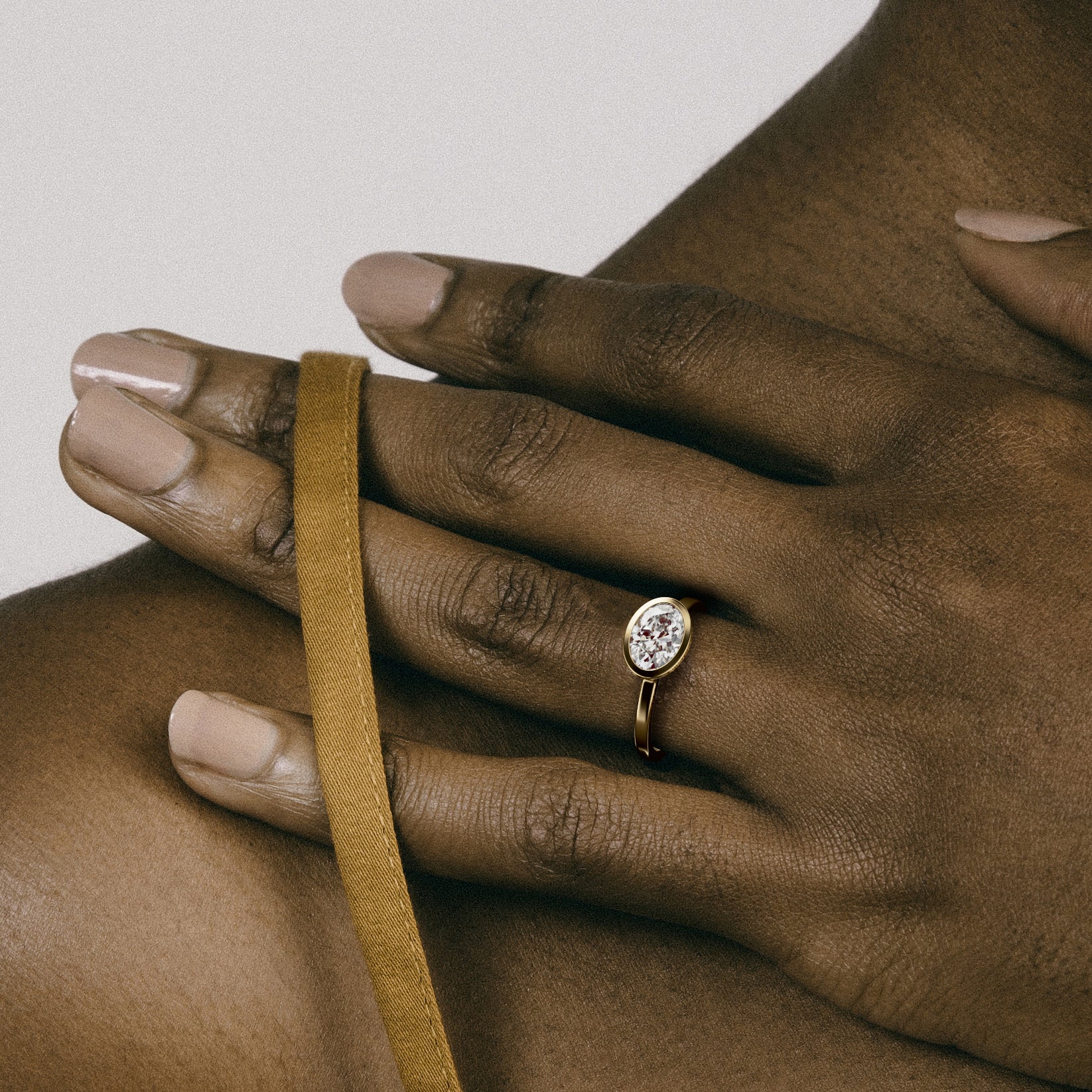 Minimal yellow gold engagement ring with bezel set oval brilliant diamond worn on hand