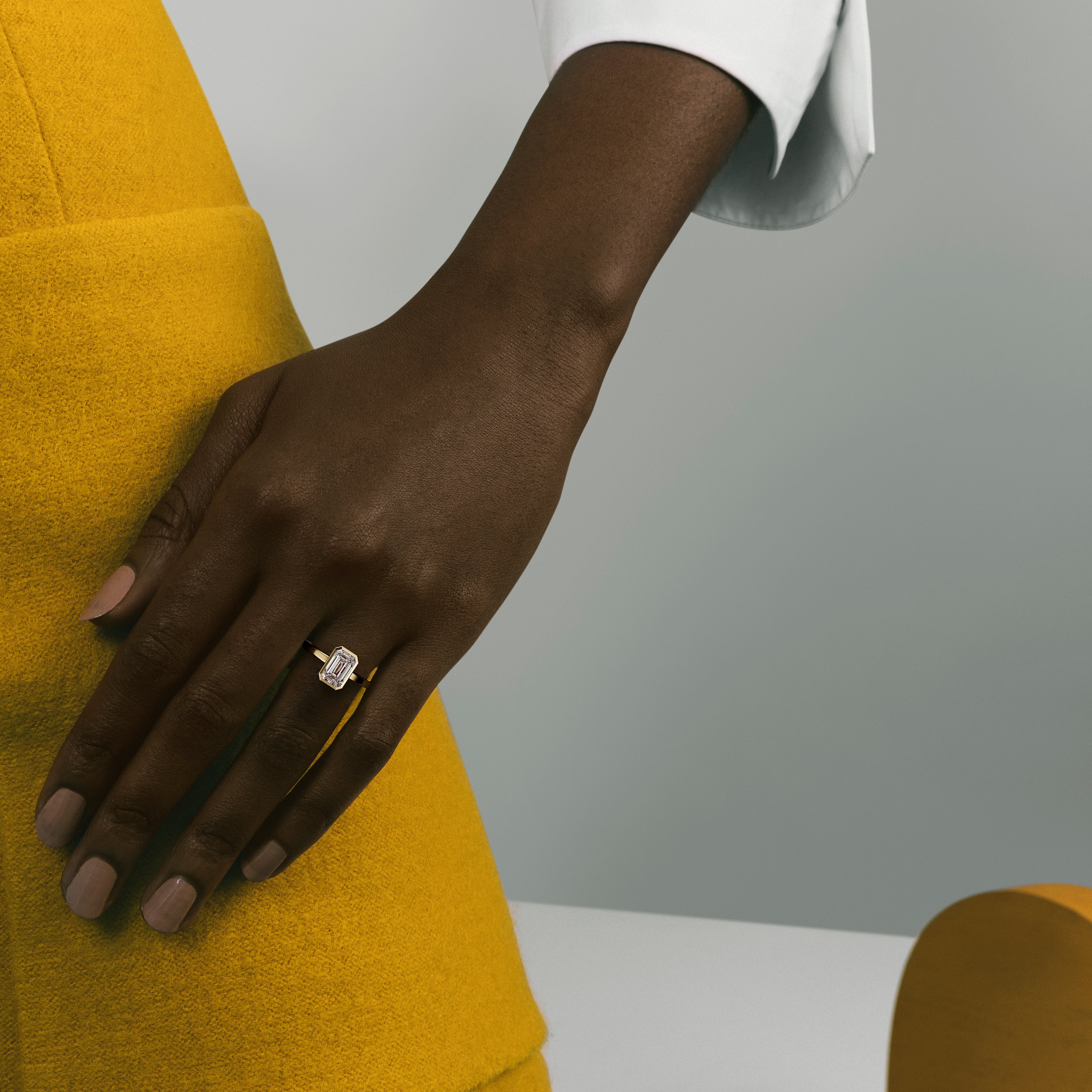 Minimal yellow gold engagement ring with bezel set emerald cut diamond worn on hand