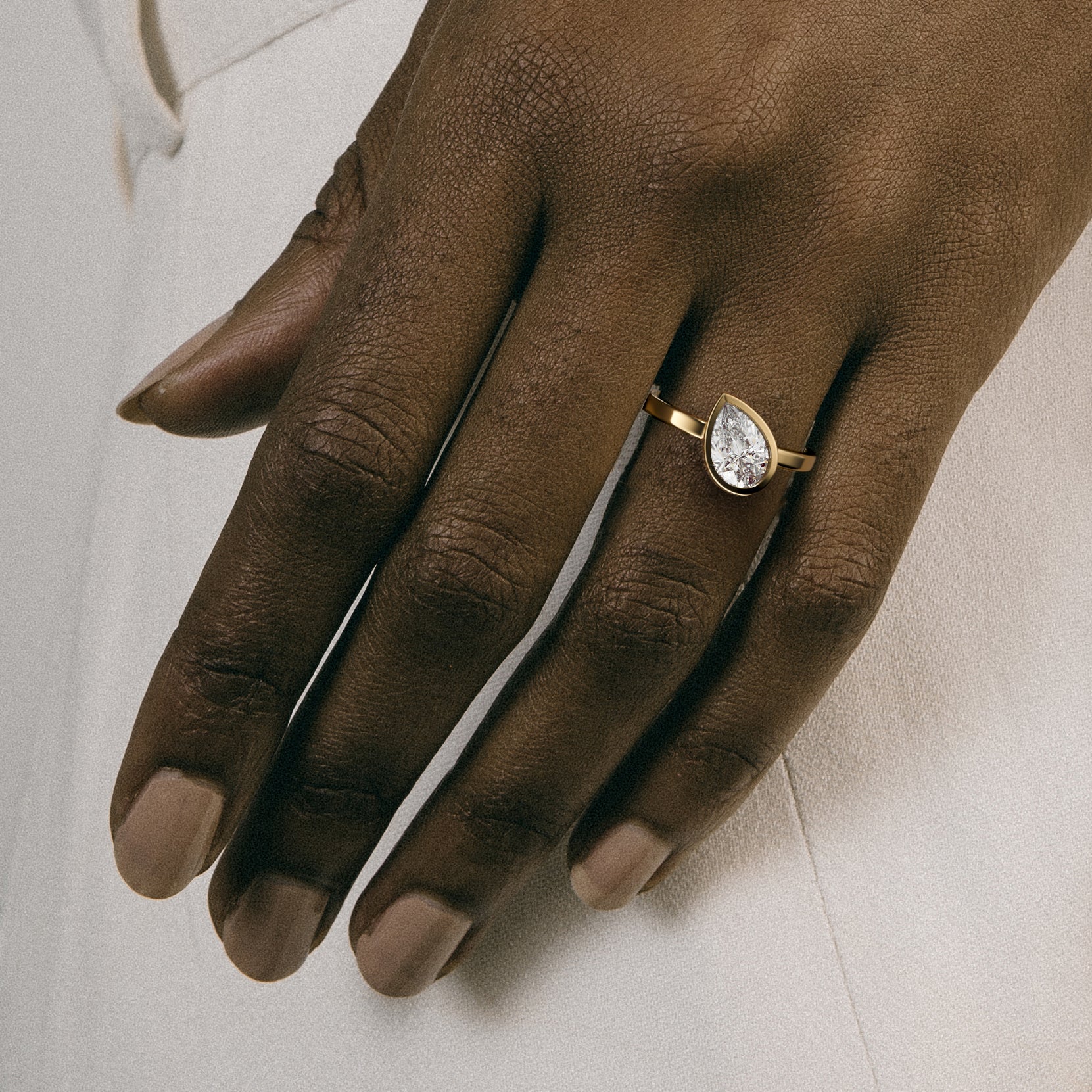 Minimal yellow gold engagement ring with bezel set pear diamond worn on hand