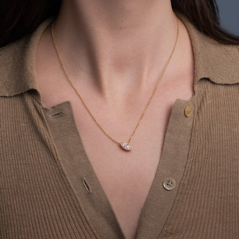 A close-up of a model wearing a delicate gold chain necklace with a marquise-cut lab-grown diamond, styled with a brown ribbed polo shirt.