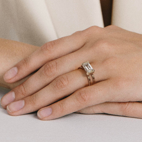 close view of east-west emerald diamond engagement ring with double band and partial bezel