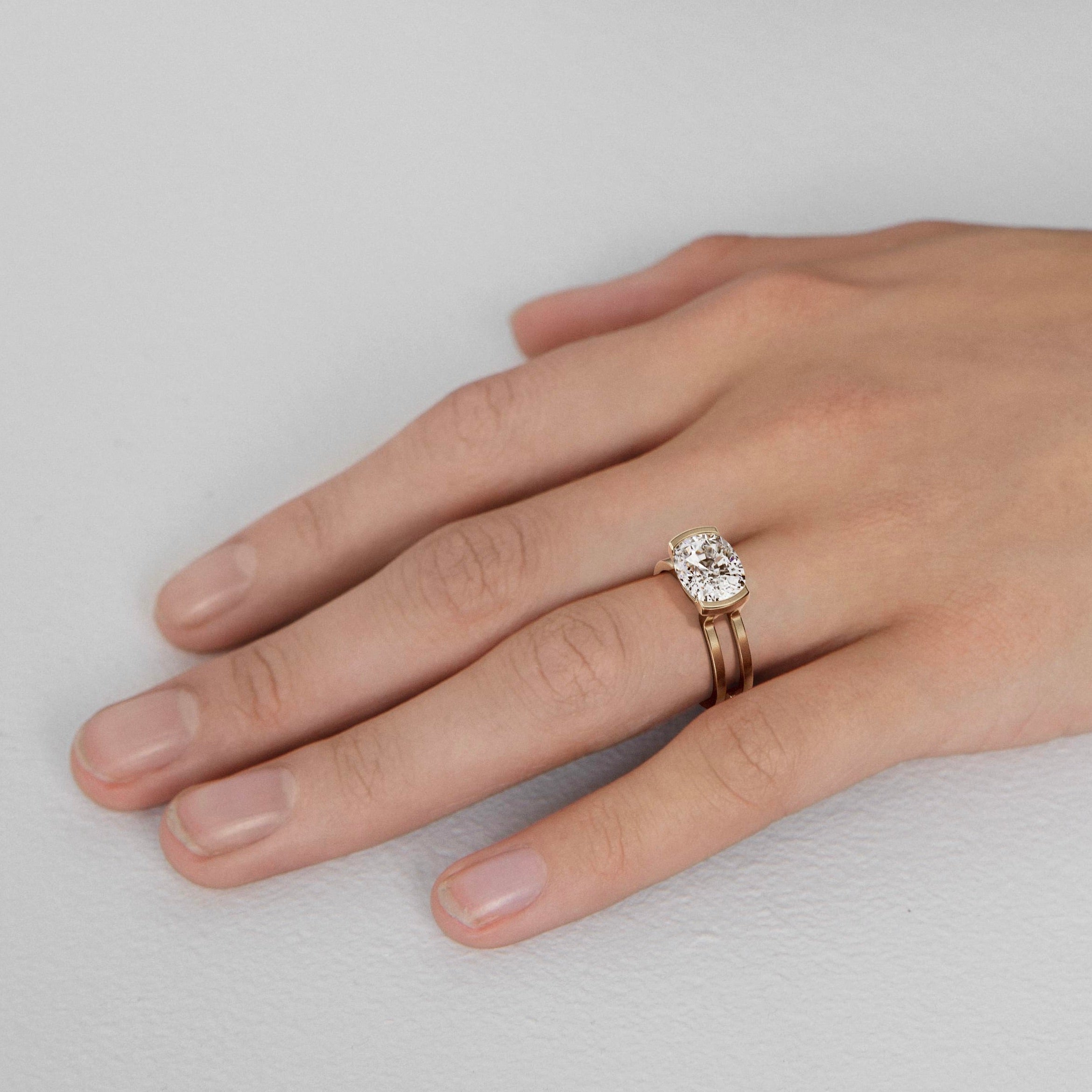 close-up of east-west cushion cut diamond engagement ring with connected double bands and partial bezel