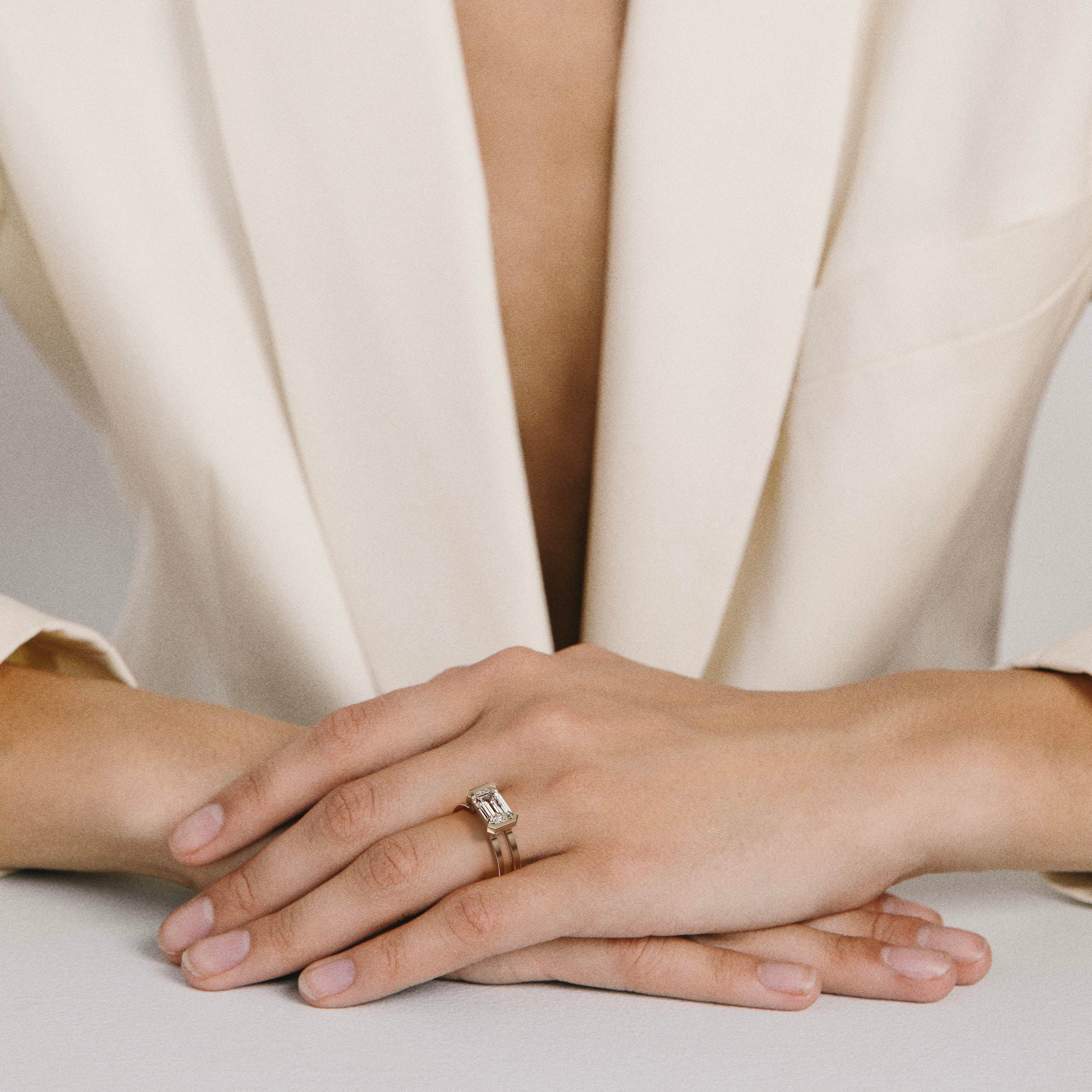 1.75 carat east-west emerald diamond engagement ring with sculptural double band worn on hand