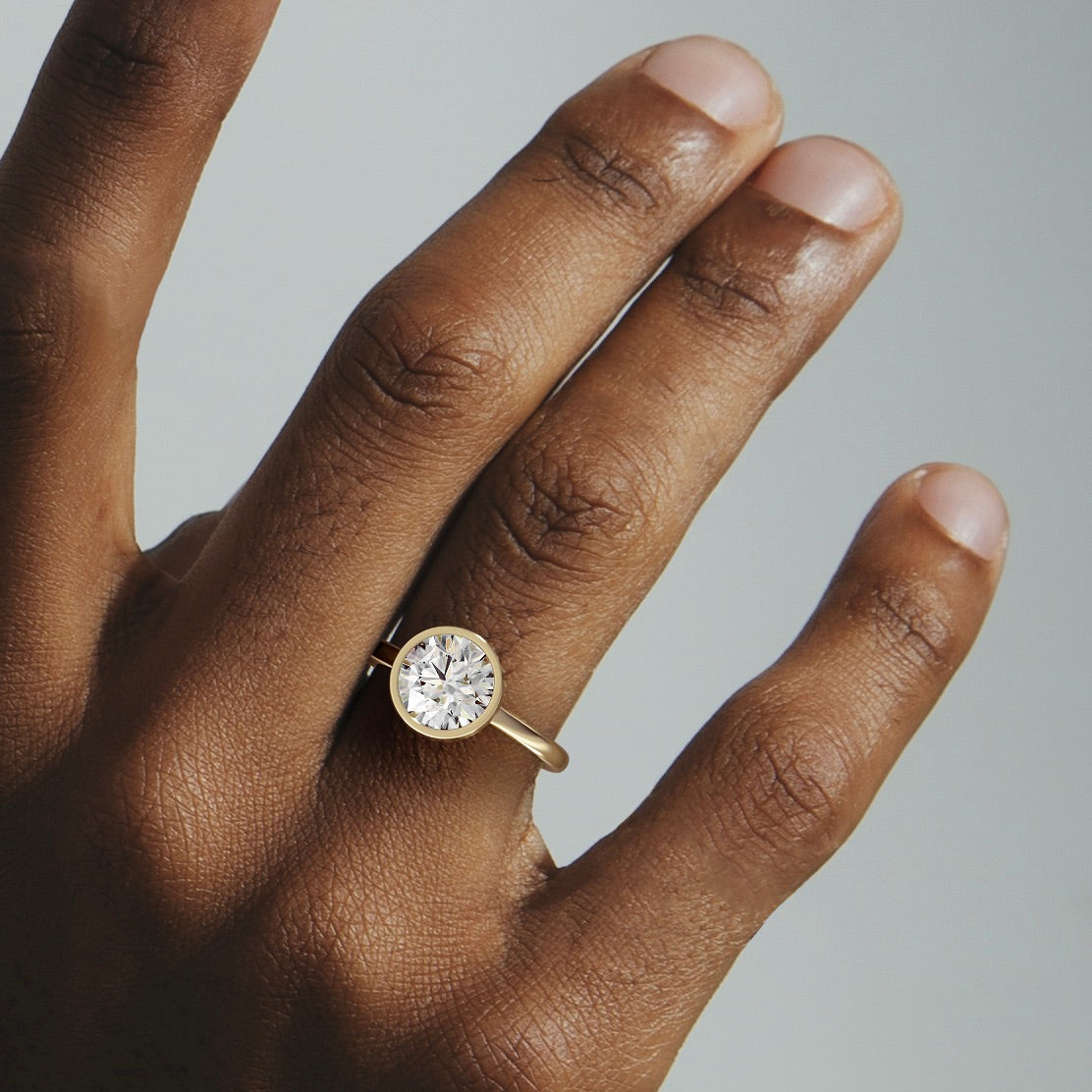 close view of 2.00 ct round brilliant diamond bezel engagement ring on thin domed band worn on hand