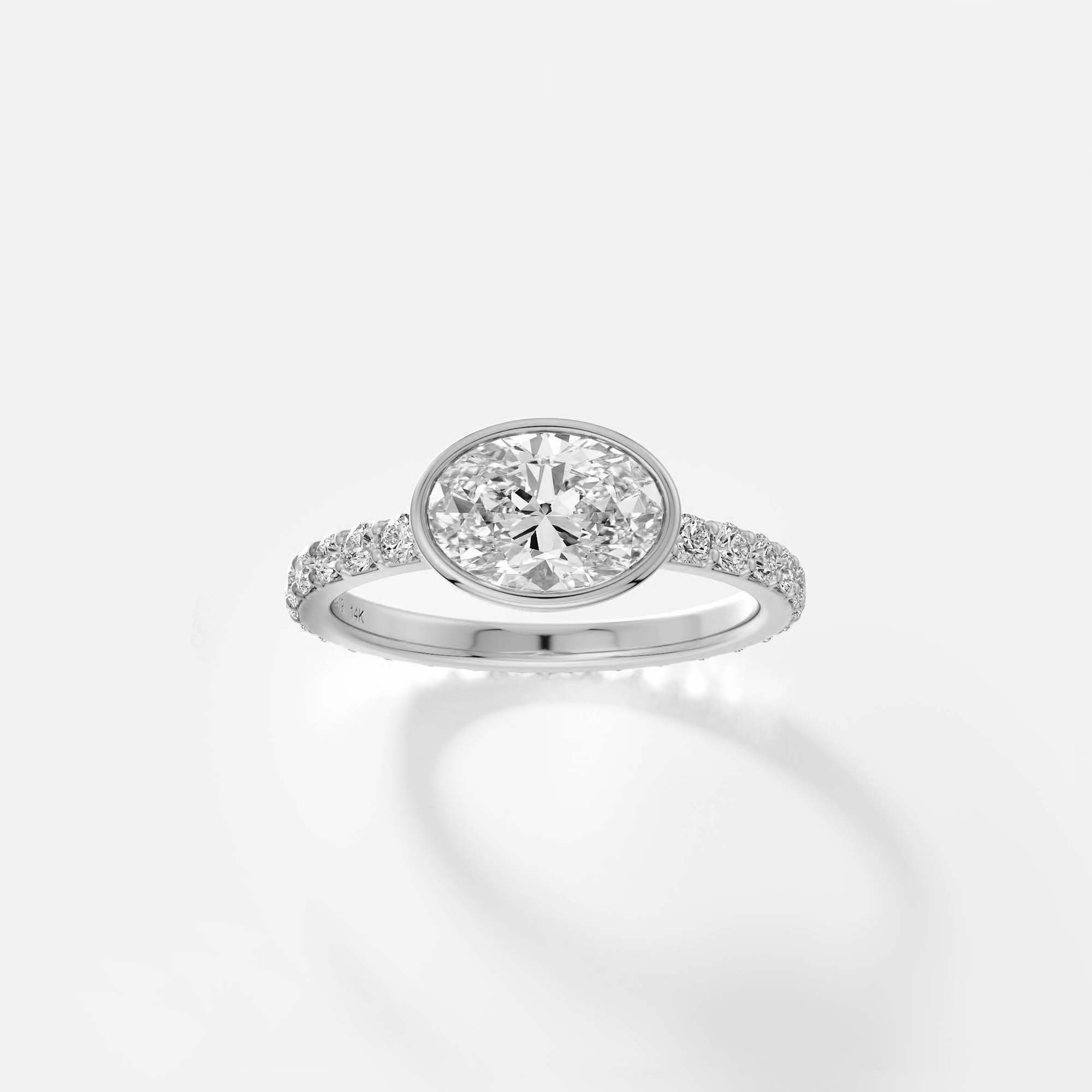 Platinum engagement ring with east-west oval diamond bezel setting and pavé diamond half eternity band