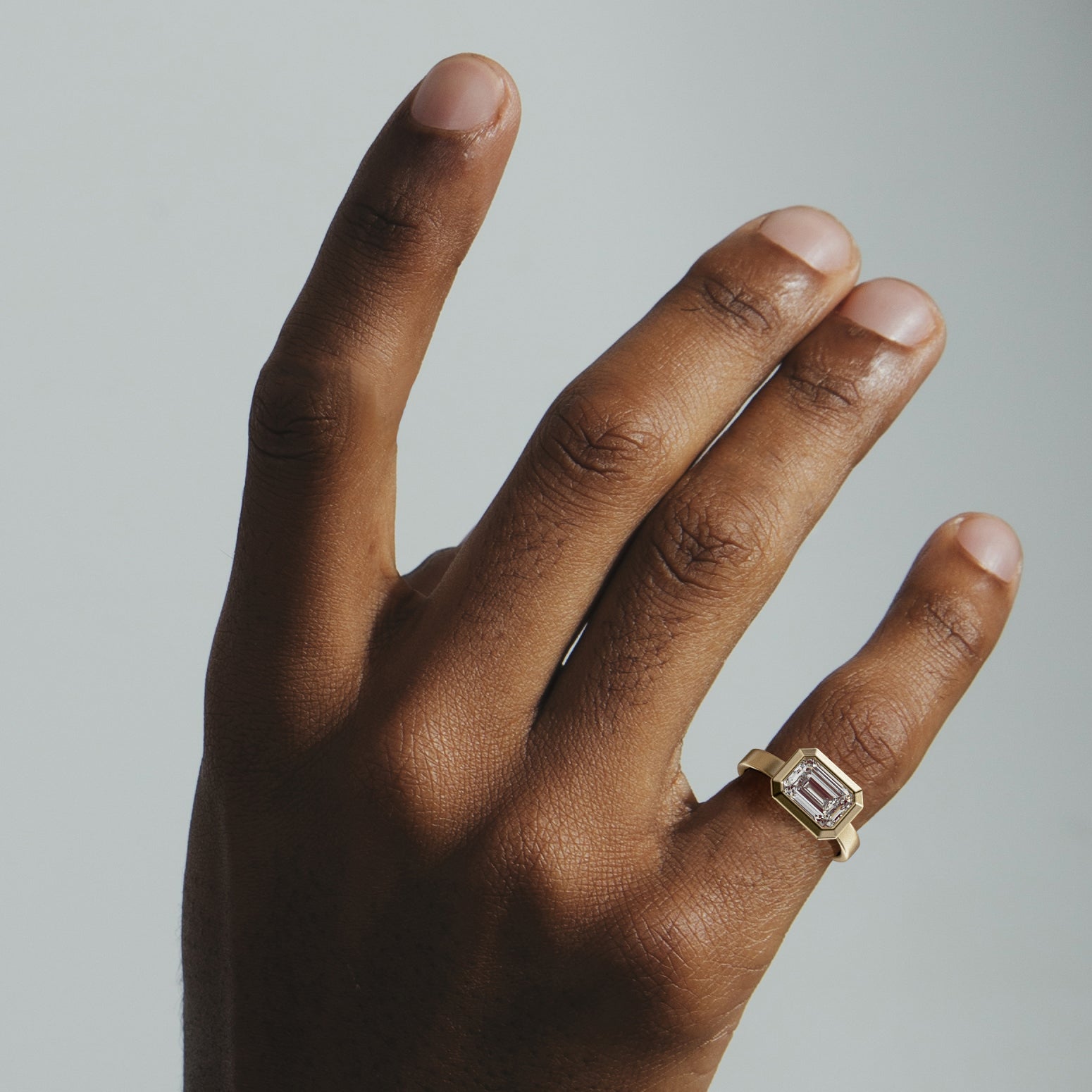 Wide band yellow gold engagement ring with emerald cut diamond facing left right worn on hand
