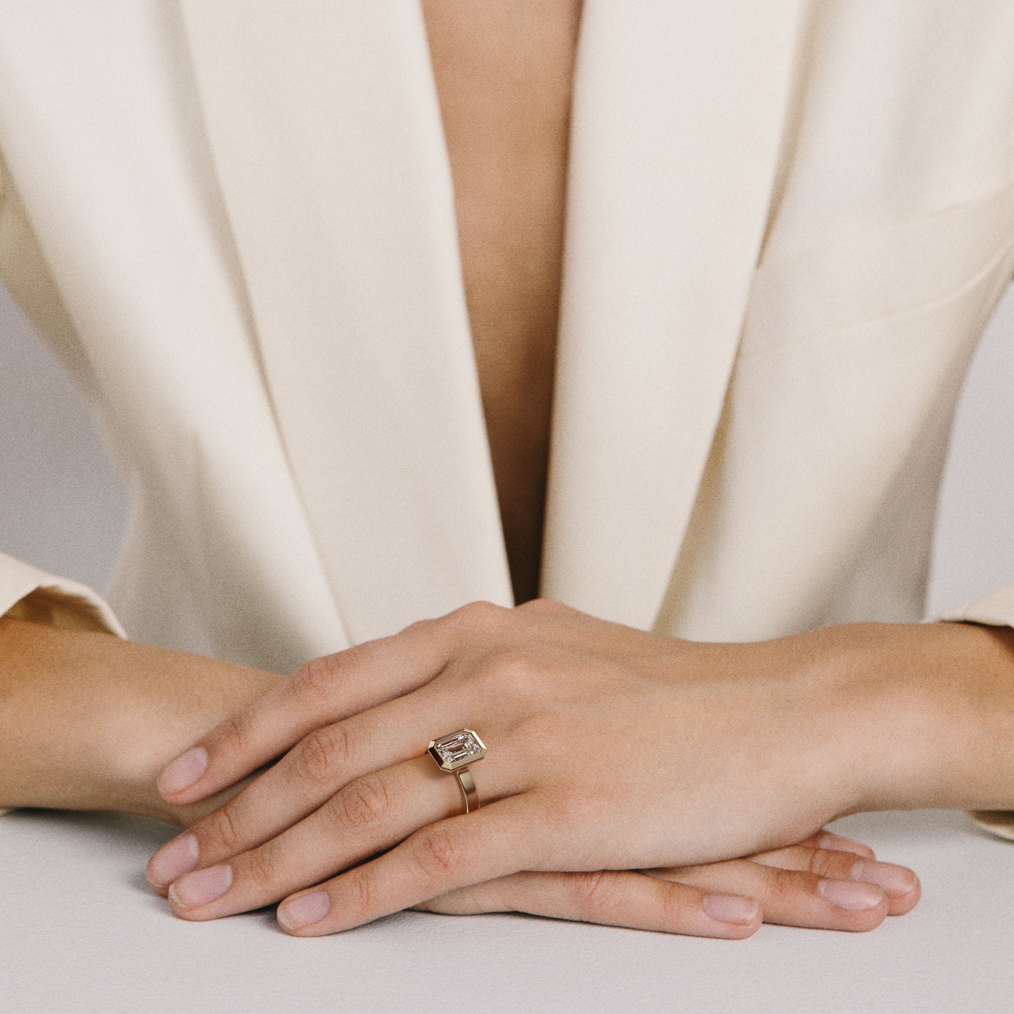 Wide band yellow gold engagement ring with emerald cut diamond worn on hand