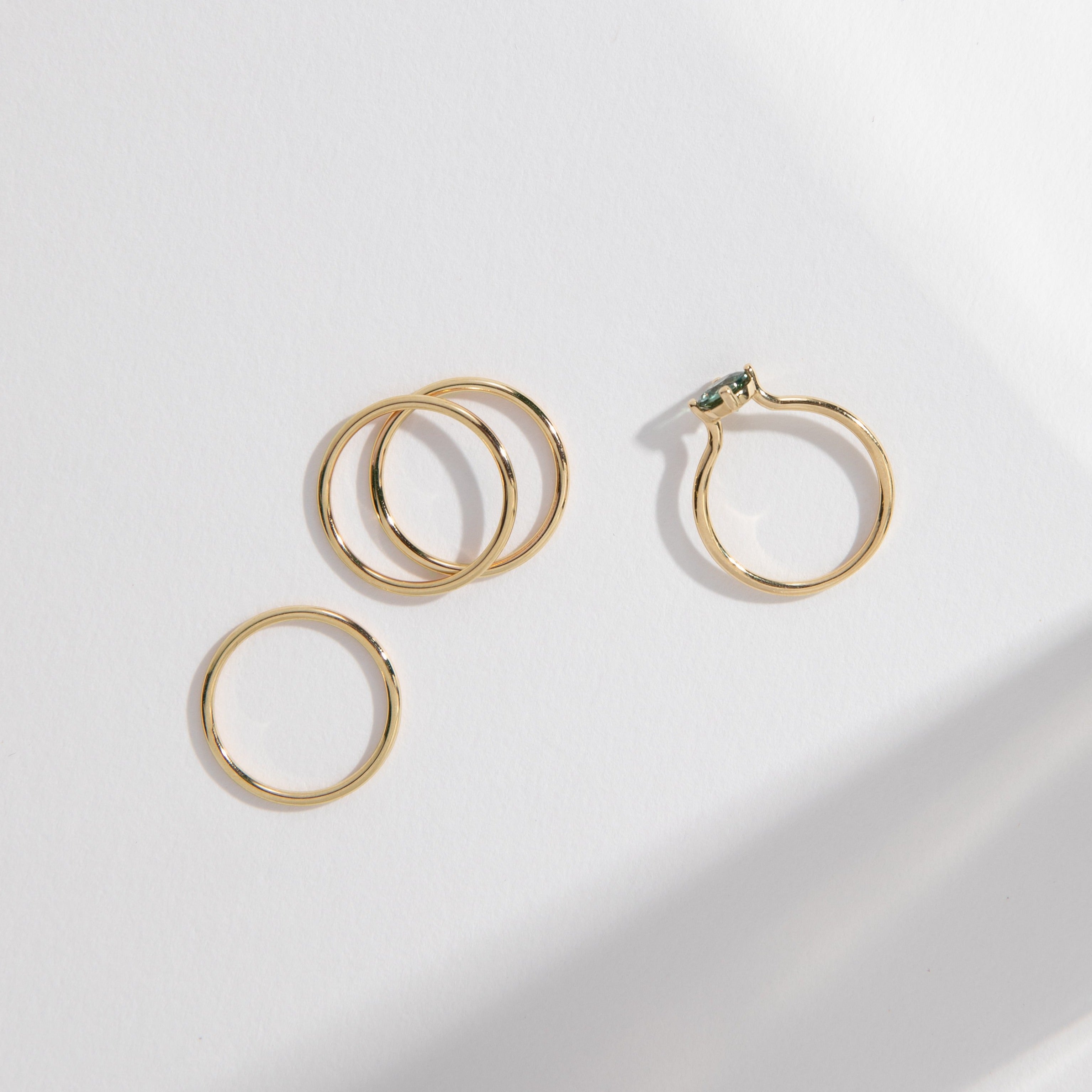 Three delicate gold bands styled alongside a sapphire engagement ring