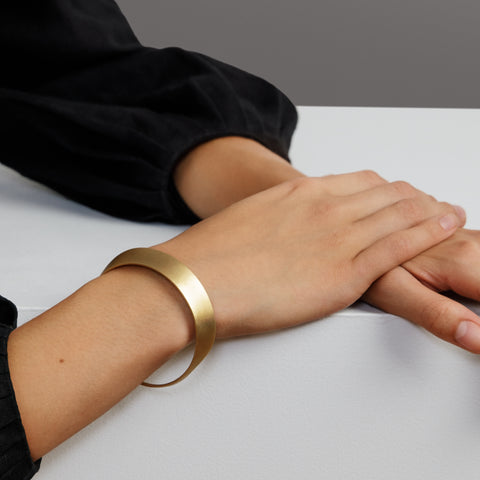 yellow brass bangle bracelet with curved sculptural form worn on wrist