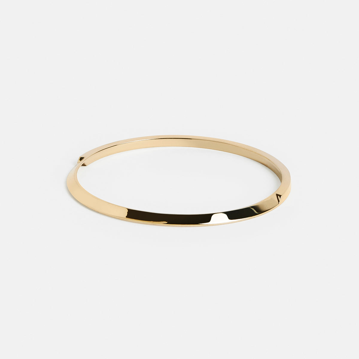 yellow brass bangle bracelet with tapered curved lines forming a structured sculptural silhouette